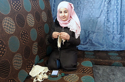 Une fille en Jordanie est en train de coudre un masque selon des instructions données par téléphone