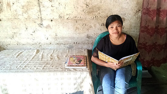 Une fille est assise devant la maison, tenant un cahier